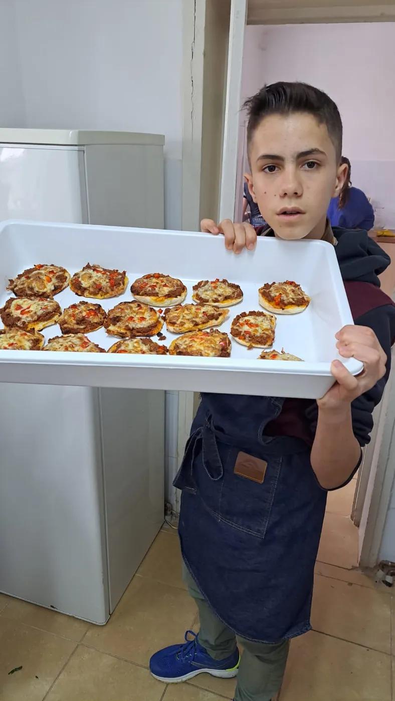 Elev ținând o tavă cu produse de brutărie coapte la atelier